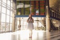 Theme travel and tranosport. Beautiful young caucasian woman in dress and backpack standing inside train station or terminal looki Royalty Free Stock Photo