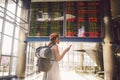 Theme travel and tranosport. Beautiful young caucasian woman in dress and backpack standing inside train station or terminal looki Royalty Free Stock Photo