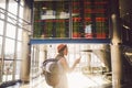 Theme travel and tranosport. Beautiful young caucasian woman in dress and backpack standing inside train station or terminal looki Royalty Free Stock Photo