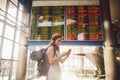 Theme travel and tranosport. Beautiful young caucasian woman in dress and backpack standing inside train station or terminal looki Royalty Free Stock Photo