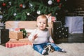 Theme winter and Christmas holidays. Child boy Caucasian blond 1 year old sitting home floor near Christmas tree with New Year dec