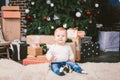 Theme winter and Christmas holidays. Child boy Caucasian blond 1 year old sitting home floor near Christmas tree with New Year dec