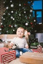 Theme winter and Christmas holidays. Child boy Caucasian blond 1 year old sitting home floor near Christmas tree with New Year dec