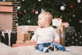 Theme winter and Christmas holidays. Child boy Caucasian blond 1 year old sitting home floor near Christmas tree with New Year dec