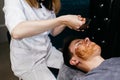 Therapist applying a face mask to a beautiful young man in a spa using a cosmetics brush. Royalty Free Stock Photo