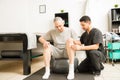 Therapist Assisting Mature Male Patient Sitting On Exercise Ball