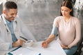 Therapist man checking hypertension of young expectant woman, measuring blood pressure for young pregnant patient