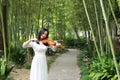 Asian Eastern Chinese young artist player woman carry play violin perform music park garden nature outdoor bamboo path Royalty Free Stock Photo