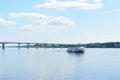 There is a boat on the river. A Seagull flies over the river. Bridge. Forest. Nature. Sunny weather. The sky, clouds scatter