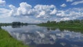 There are bushes and willows growing on the grassy banks of the river. On the water - ripples and reflection of trees, blue sky an Royalty Free Stock Photo