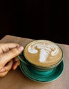 There is a cup of cappuccino on Kraft paper and it is held by a man`s hand, at the top of the frame there is plenty of space