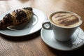 There is a cup of cappuccino on an oak table.