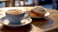 There is a cup of cappuccino on a wooden table and a Cinnabone bun on a saucer next to it