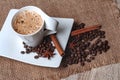 There is a cup of coffee and a saucer on the table.On the saucer are coffee beans, a cinnamon stick and anise star. Royalty Free Stock Photo