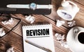 There is a cup of coffee on a wooden table, a clock, glasses and a notebook with the word REVISION. Business concept Royalty Free Stock Photo