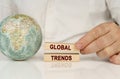 There is a globe on a white reflective surface, in the hands of wooden blocks with the inscription - GLOBAL TRENDS