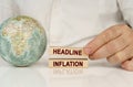 There is a globe on a white reflective surface, in the hands of wooden blocks with the inscription - HEADLINE INFLATION