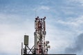 There is a gray and red Radio relay tower with group of different cellular and satellite antennas on the blue sky with white