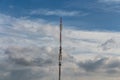 There is a gray and red Radio relay tower with group of different cellular and satellite antennas on the blue sky with white