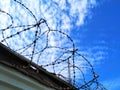 Iron fence gray. On top of wound barbed wire with spikes. Against a blue sky with clouds Royalty Free Stock Photo