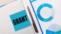 There is a pen between the blue sticky note with the text GRANT and the blue chart. Business concept. View from above Royalty Free Stock Photo