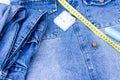 There are sewing supplies on top of the denim items. A centimeter, threads, pins and a thimble lie on things