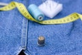 There are sewing supplies on top of the denim items. A centimeter, threads, pins and a thimble lie on things