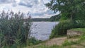 There are trees on the sandy and grassy shore of the lake, and there are reeds in the water next to it. On the opposite shore is a Royalty Free Stock Photo