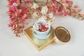 There White and Pink Branches of Chestnut Tree,Goden Present Box with Bottle Cream are on White Table