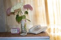 There is a wired telephone, an alarm clock and a bouquet of hydrangeas