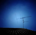 Silhouette of TV antenna installed on roof with dark blue sky background.