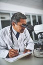 Theres no limit to his medical expertise. a mature scientist using a microscope and recording his findings in a