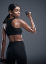 Theres no underestimating her strength. Studio portrait of a sporty young woman lifting weights against a grey