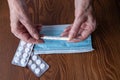 Thermometer in the hands of an elderly woman. Pills, mask. Medicines on a wooden background