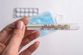 thermometer in the hands of a woman. Pills and a medical mask on the table. Close-up