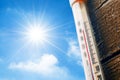 Thermometer with a high temperature reading on a scale, against a background of bright sun and a blue sky with clouds. The concept Royalty Free Stock Photo