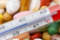 Thermometer indicating a temperature over 40ÃÂ°C. Background of tablets, capsules and pills of different kinds and colors Royalty Free Stock Photo