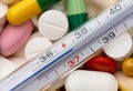 Thermometer indicating a temperature of 37 ÃÂ°C. Background of tablets, capsules and pills of different kinds and colors