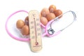 The thermometer laying on eggs with pink stethoscope. Food and h