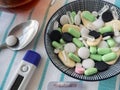 Thermometer, many different medications in a small plate, a tablet in a spoon close-up. The treatment of the disease.