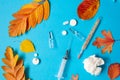 Thermometer, syringe, ampoules, pills, crumpled paper napkin and yellow fallen leaves on blue paper background. Thermometer has