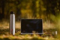 Thermos with cup near laptop with free space on moss in forest Royalty Free Stock Photo