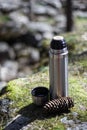 Thermos, cup and pinecone- picnic on mossy rock