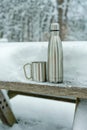 Thermos flask with drinking cup on a snow-covered table