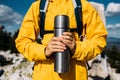 A thermos in the hands of a traveler. A man in tourist clothes with a thermos of coffee or tea in his hand against the background Royalty Free Stock Photo