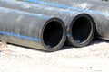 Thick black rubber pipes left on gravel road at local construction site waiting to be installed