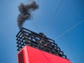 Thick black smoke leaves the exhaust on a ship with surrounding black superstructure. Taken on a sunny day with a blue sky