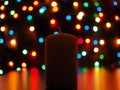 Thick candle and colorful bokeh on a black background.