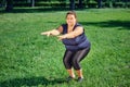 Thick caucasian woman doing gymnastic exercises in park.