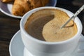 Thick foam of hot coffee cappuccino with spoon in white cup and croissant on wooden table, closeup. Milk foam cappuccino, latte Royalty Free Stock Photo